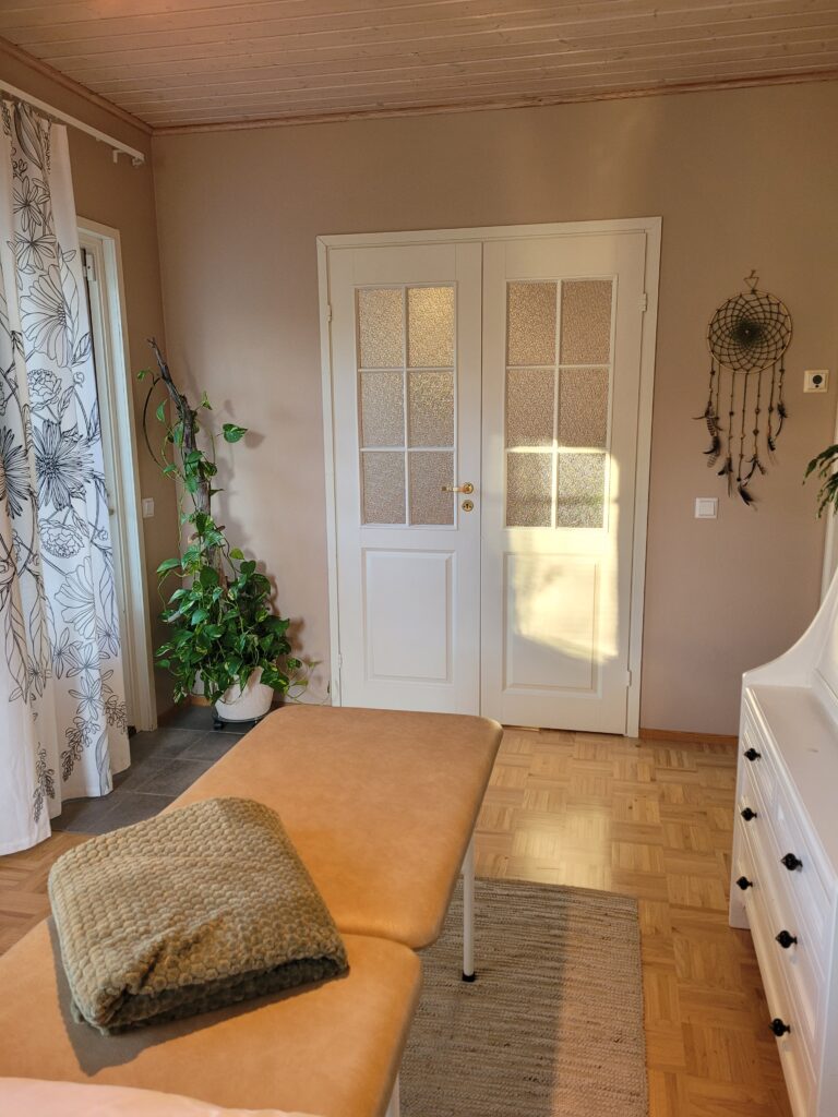 Hoitohuone, jossa näkyy hoitopöytä ja ovet. Hoitopöydällä on viltti.