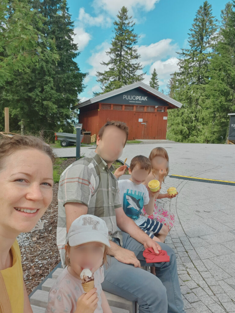 Slesar-perhe jäätelöllä Puijontornin aukiolla Kuopiossa. Perheenisän ja lasten kasvot sumennettu. Äiti etualalla.